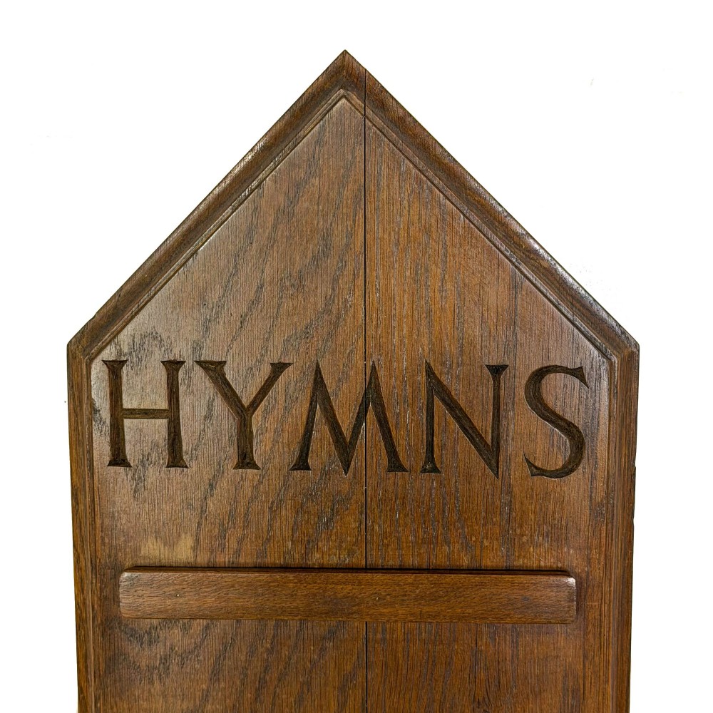 An antique solid oak hymn board featuring a pointed arched top with the word HYMNS cut out above five horizontal display slots. View III