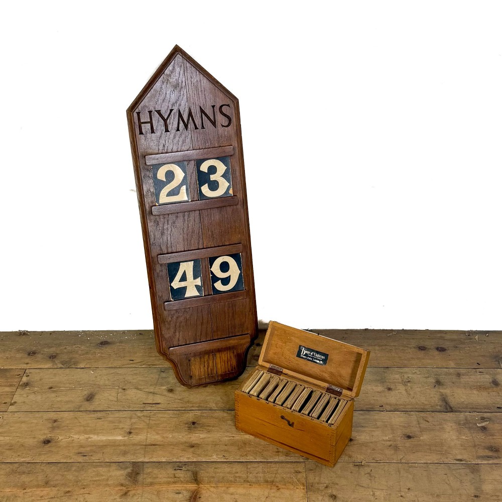 An antique solid oak hymn board featuring a pointed arched top with the word HYMNS cut out above five horizontal display slots. View VII