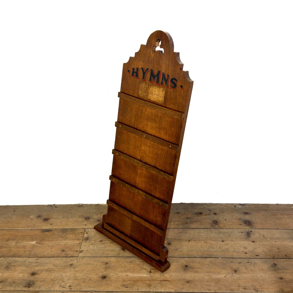 An antique dark oak church hymn board featuring a trefoil cutout at the carved top, painted text reading HYMNS, multiple horizontal slots, and an accompanying wooden box. View II