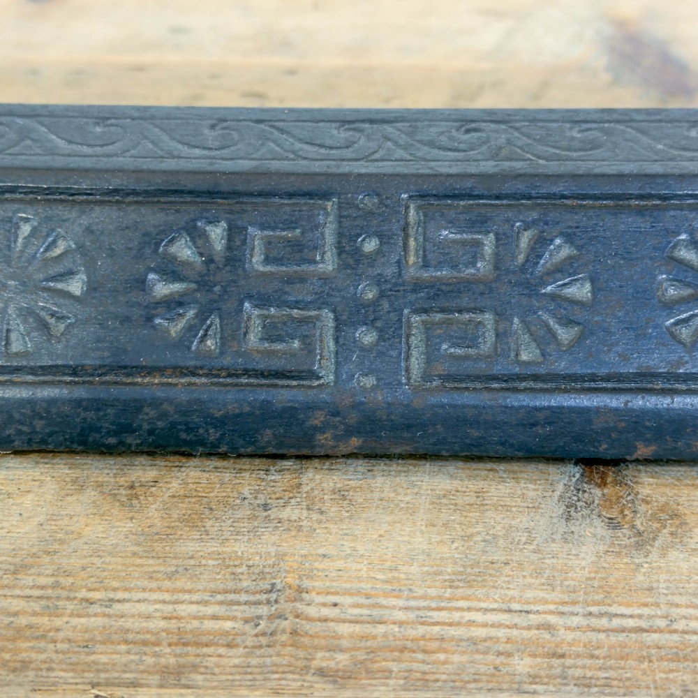 An antique Victorian fireplace fender featuring a dark metal base with stamped geometric patterns and an elevated brass rail supported by ribbed finials. View II