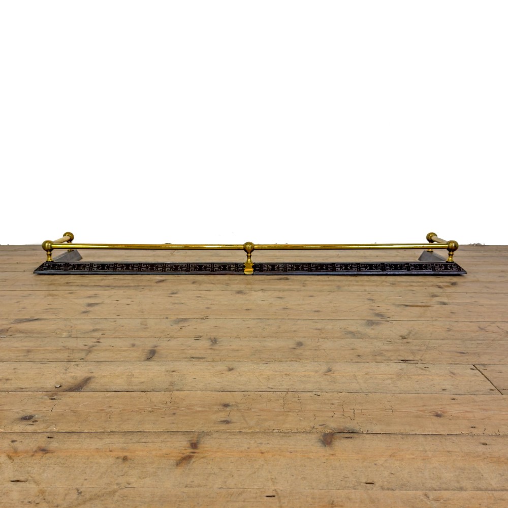 An antique Victorian fireplace fender featuring a dark metal base with stamped geometric patterns and an elevated brass rail supported by ribbed finials. View III