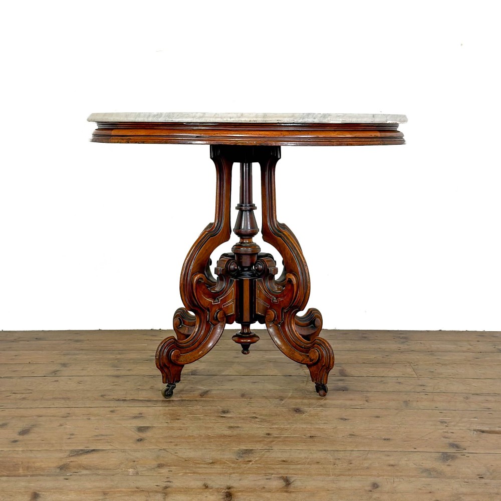 A circular Victorian side table featuring a white marble top supported by a carved mahogany pedestal base with scrolled legs.