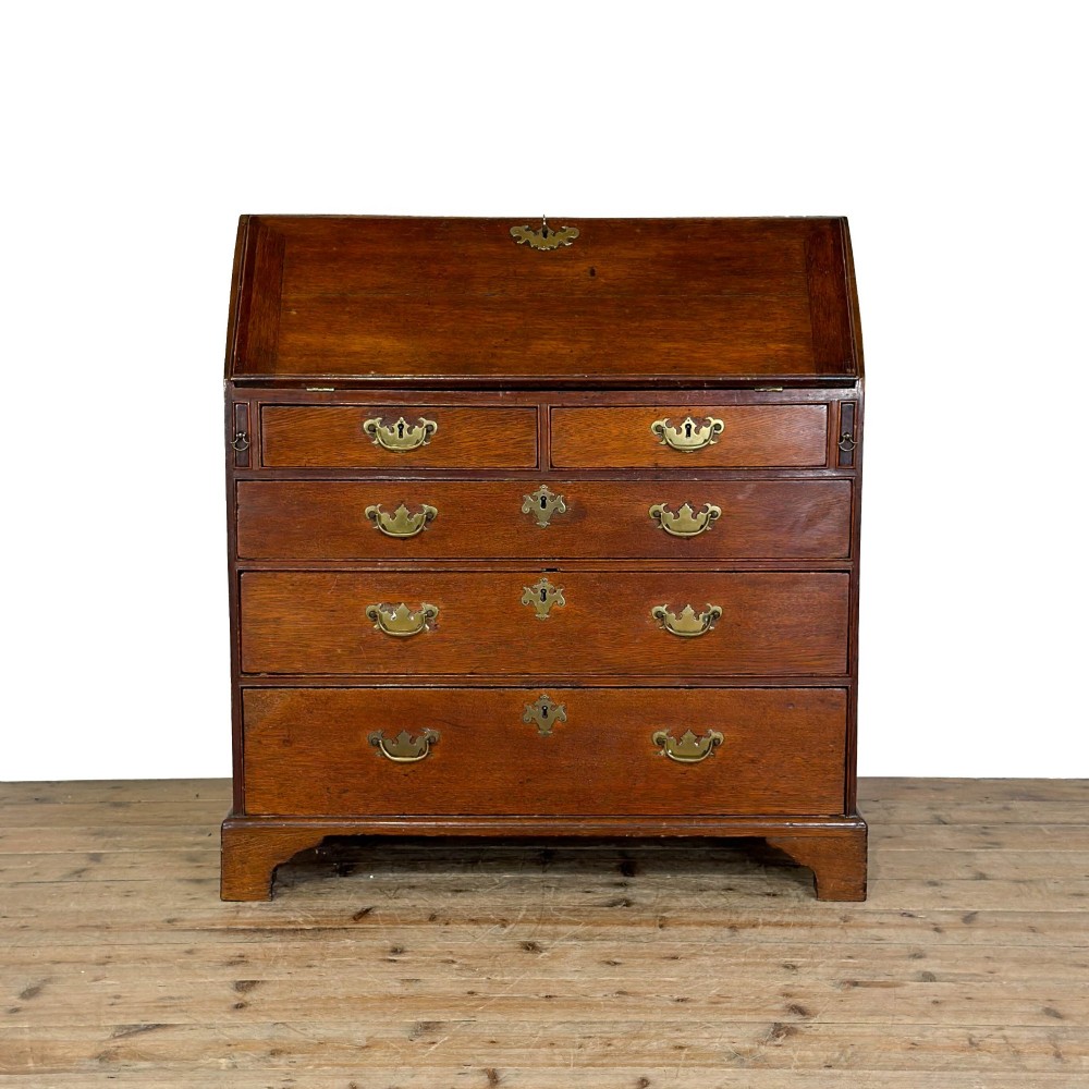 An 18th-century oak writing bureau featuring a sloping fall front above four graduated drawers with brass handles and bracket feet.