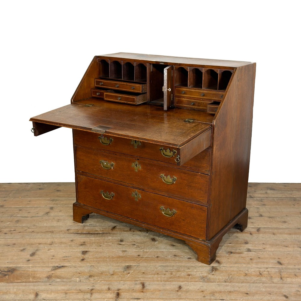 An 18th-century oak writing bureau featuring a sloping fall front above four graduated drawers with brass handles and bracket feet. View V