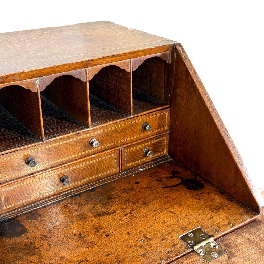 An 18th-century oak writing bureau featuring a sloping fall front above four graduated drawers with brass handles and bracket feet. View VI