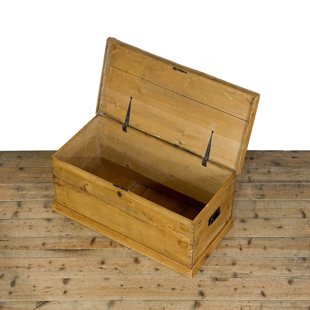 A rectangular stripped pine trunk displaying visible dovetail joints, a brass keyhole escutcheon, and a simple plinth base. View V