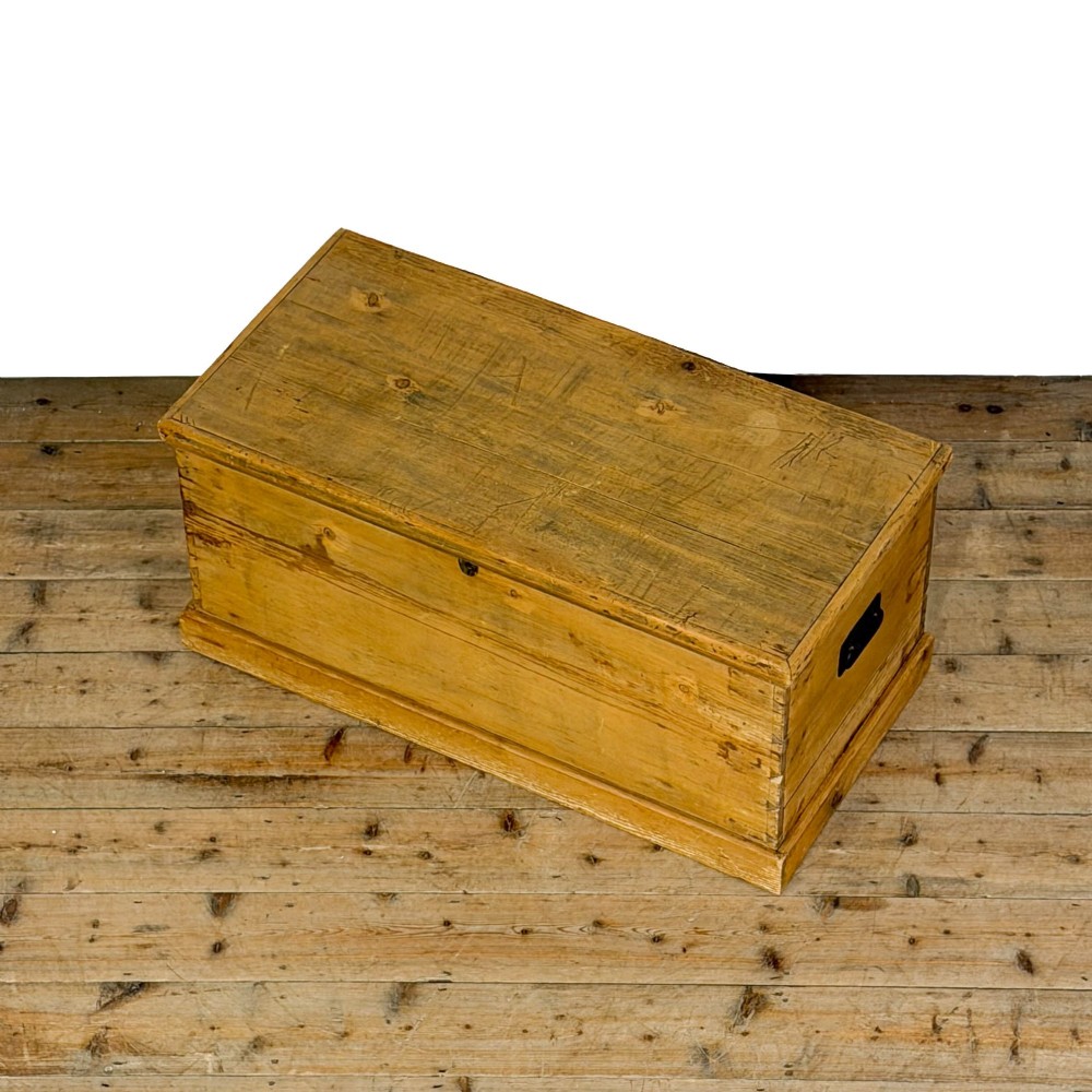 A rectangular stripped pine trunk displaying visible dovetail joints, a brass keyhole escutcheon, and a simple plinth base. View VI