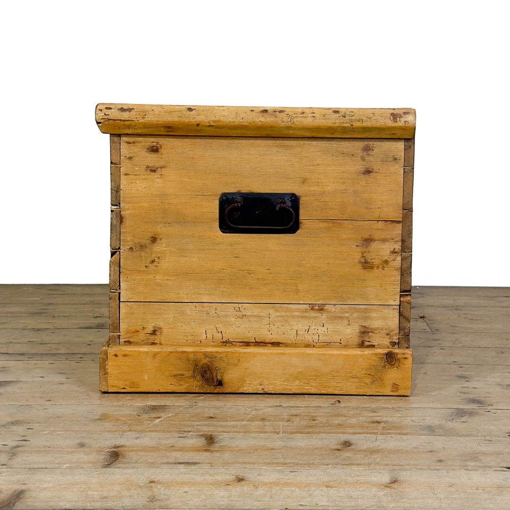 A rectangular stripped pine trunk displaying visible dovetail joints, a brass keyhole escutcheon, and a simple plinth base. View VII