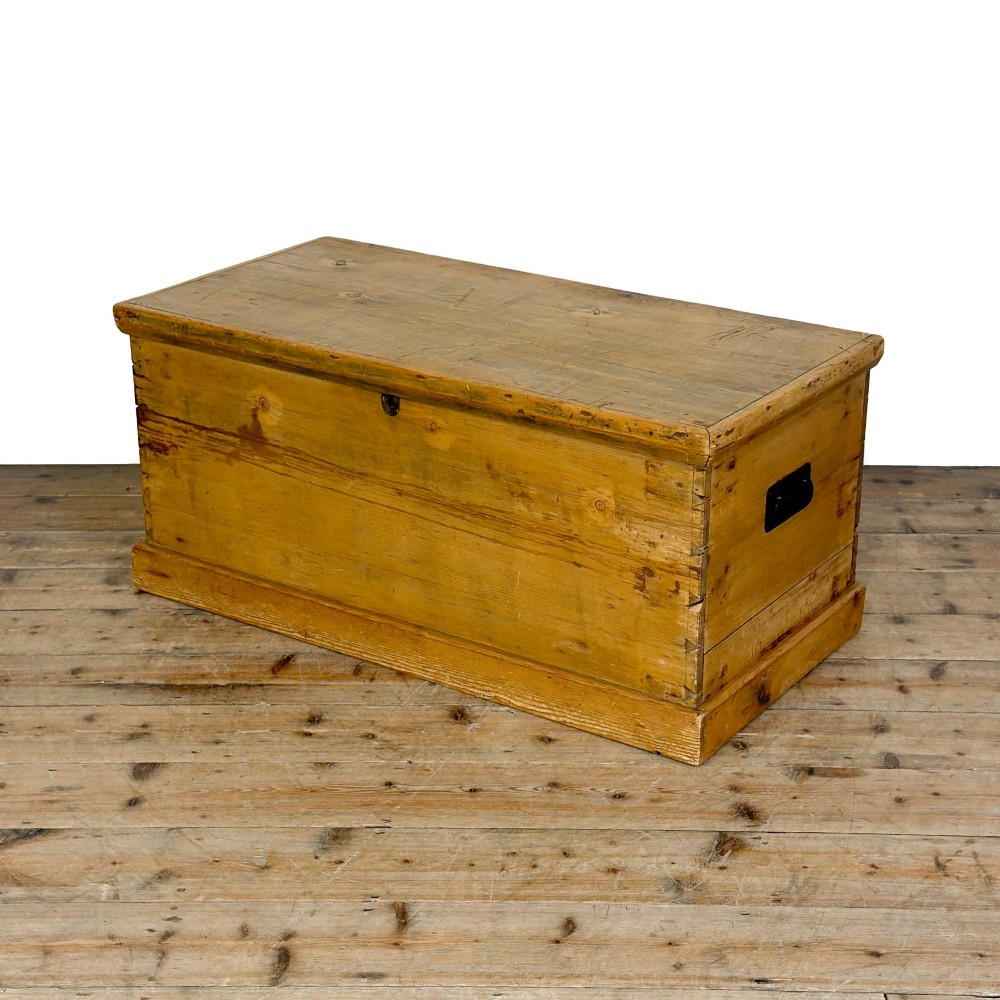 A rectangular stripped pine trunk displaying visible dovetail joints, a brass keyhole escutcheon, and a simple plinth base. View X