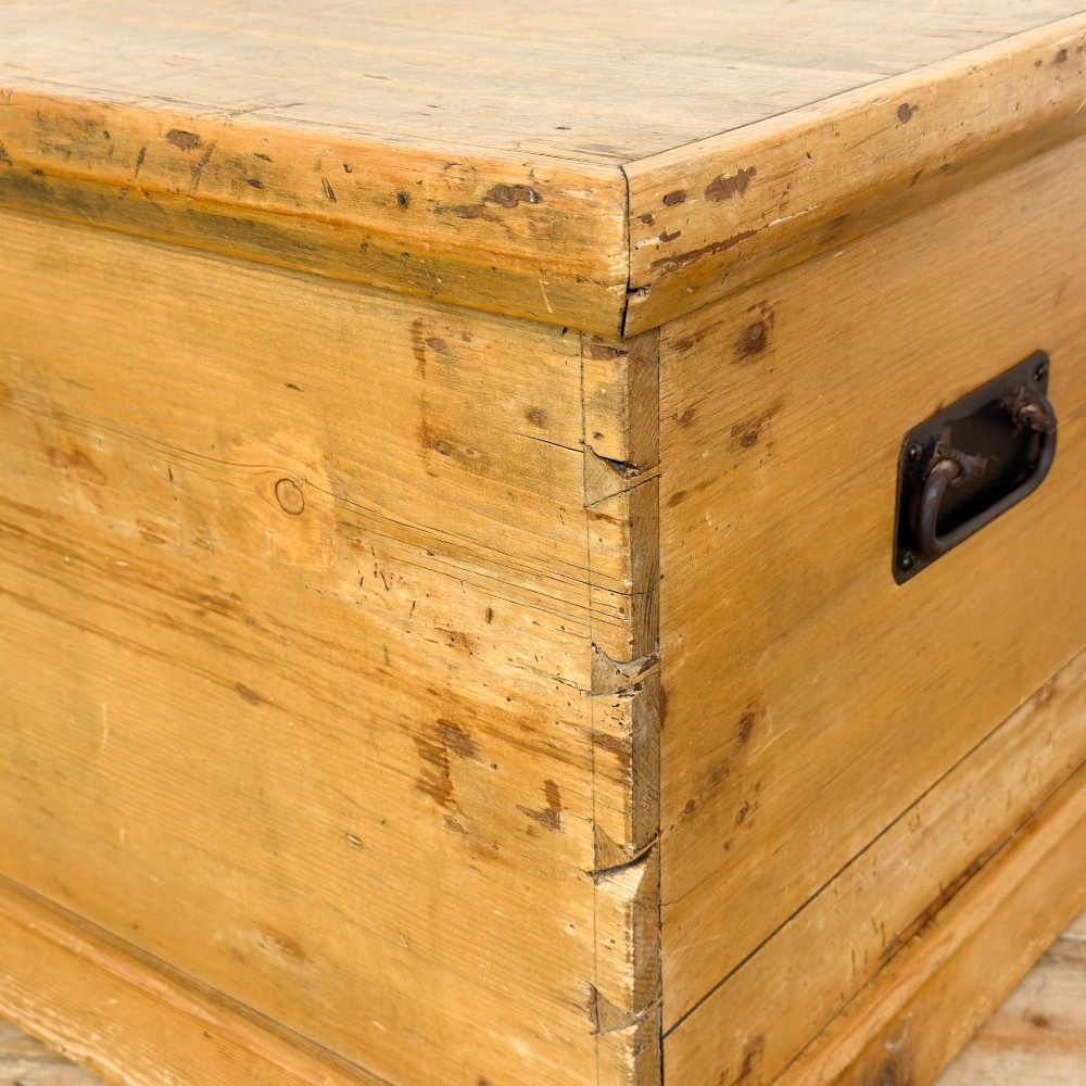 A rectangular stripped pine trunk displaying visible dovetail joints, a brass keyhole escutcheon, and a simple plinth base. View XI