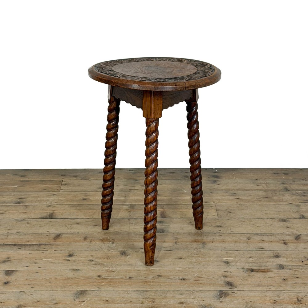 A small circular dark oak cricket table featuring a relief-carved top border and three spiral barley twist tripod legs.