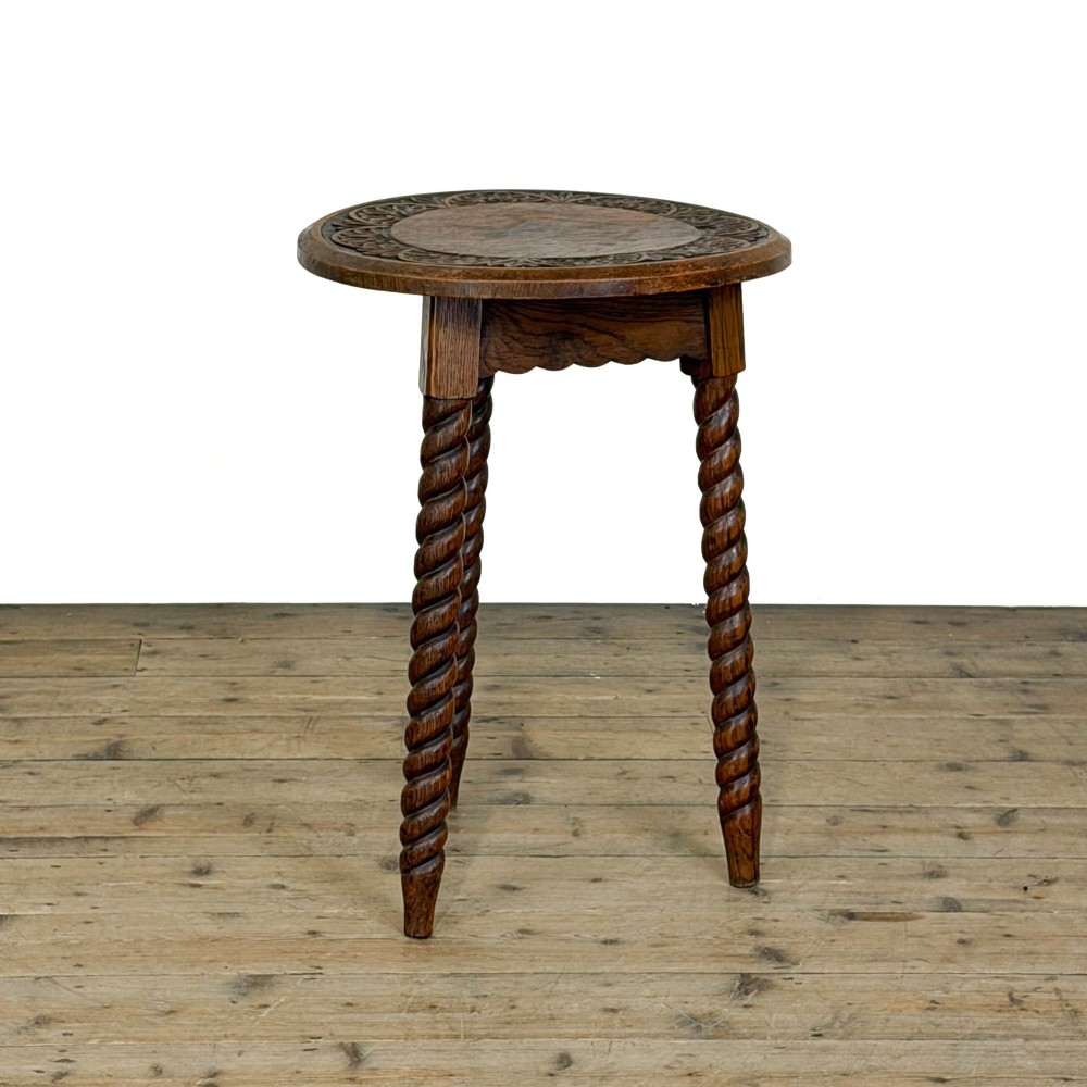 A small circular dark oak cricket table featuring a relief-carved top border and three spiral barley twist tripod legs. View II