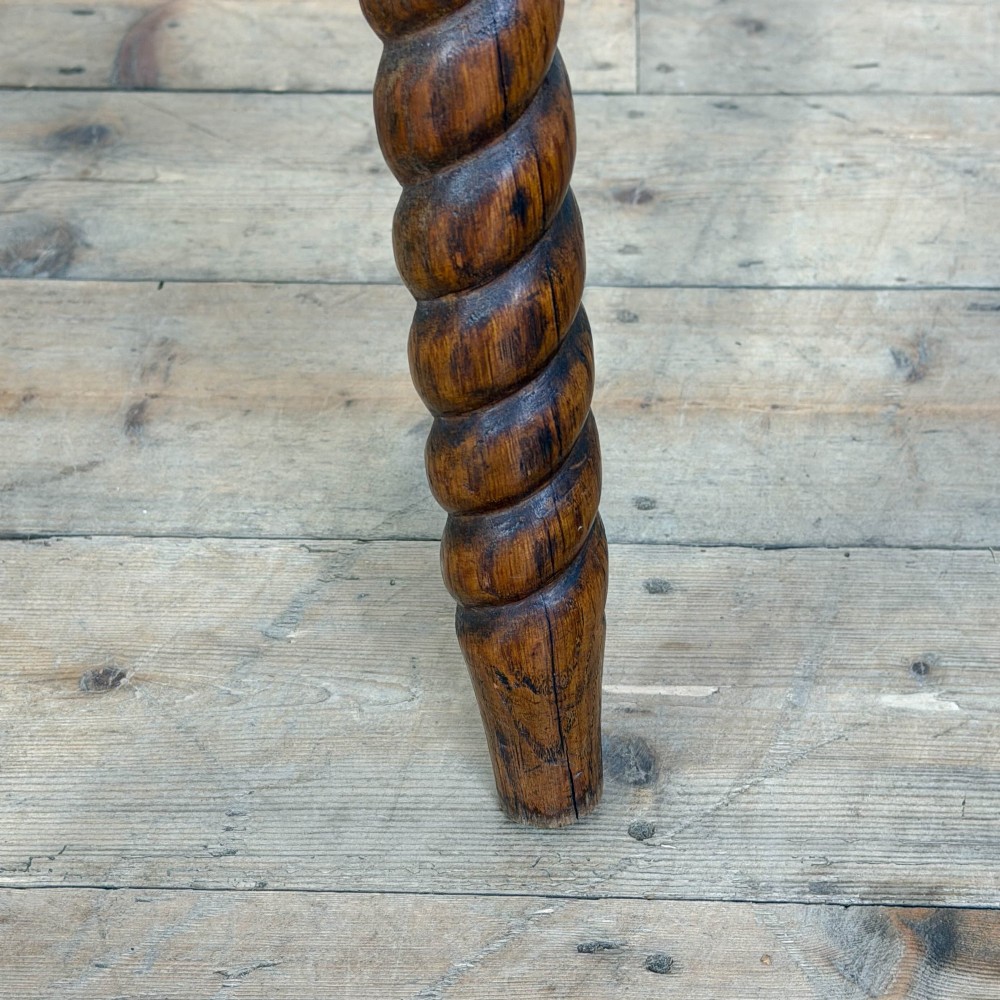 A small circular dark oak cricket table featuring a relief-carved top border and three spiral barley twist tripod legs. View V