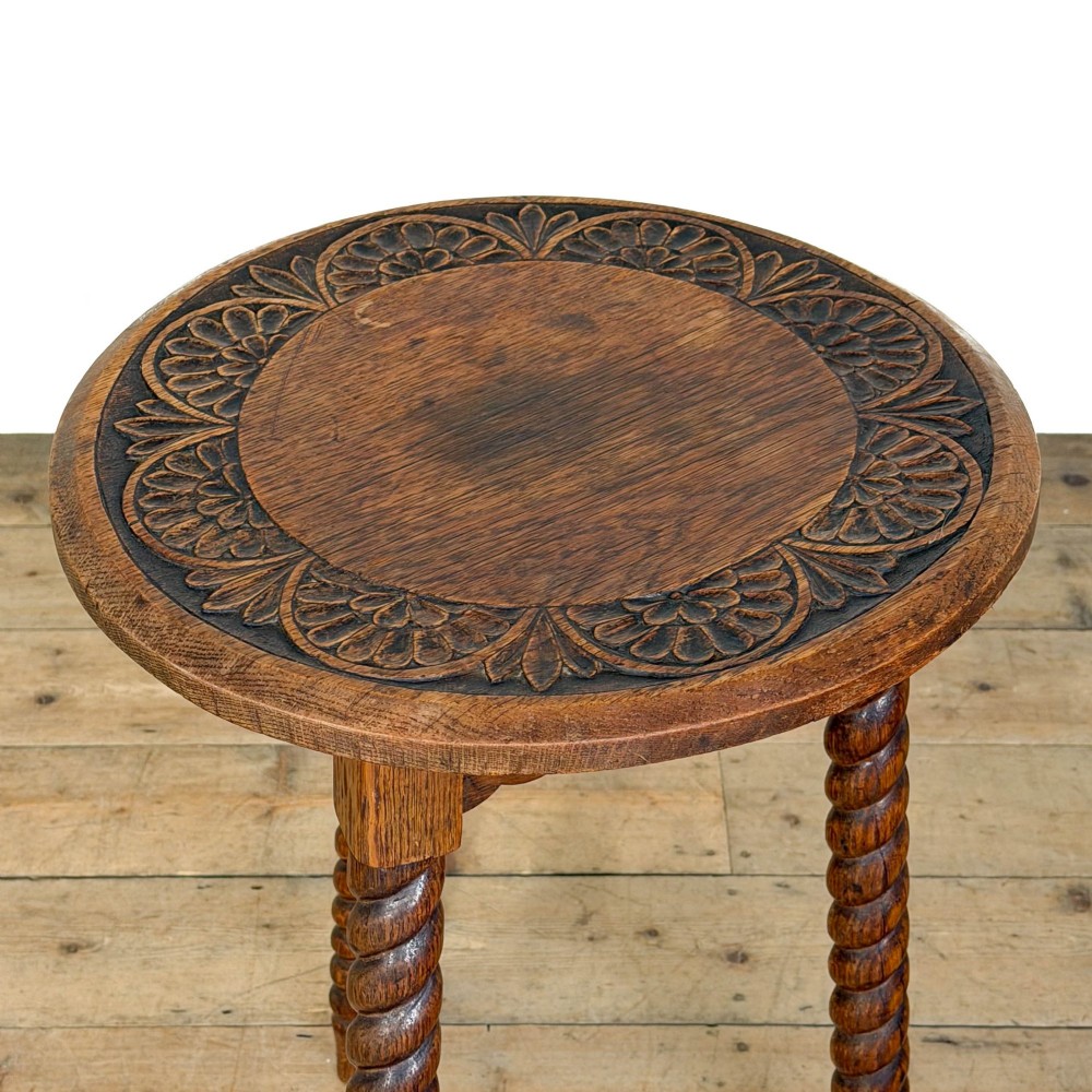 A small circular dark oak cricket table featuring a relief-carved top border and three spiral barley twist tripod legs. View VII