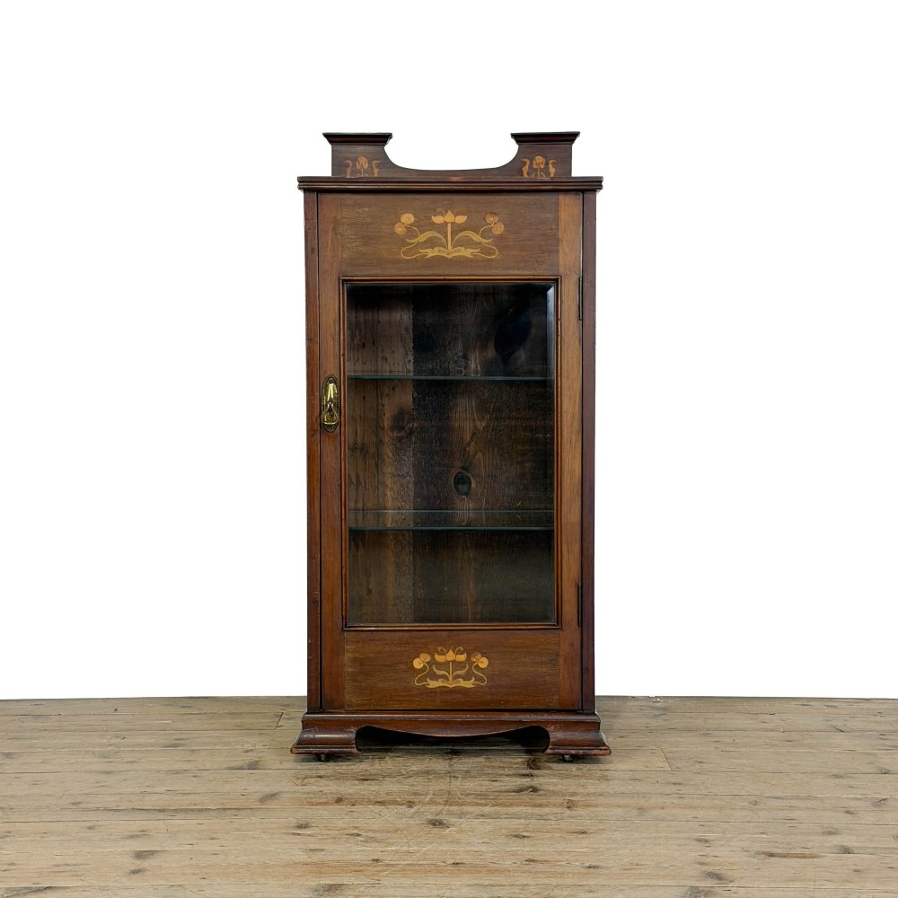 An antique dark wood Art Nouveau display cabinet featuring floral marquetry inlays, a single glazed glass door, and a shaped cresting gallery.
