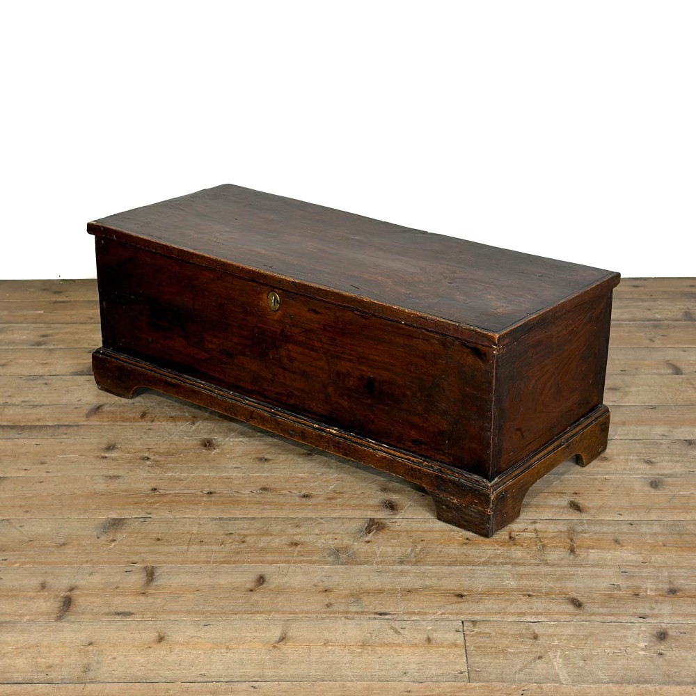A rectangular George III dark elm blanket chest with a hinged lid, brass escutcheon, and bracket feet.