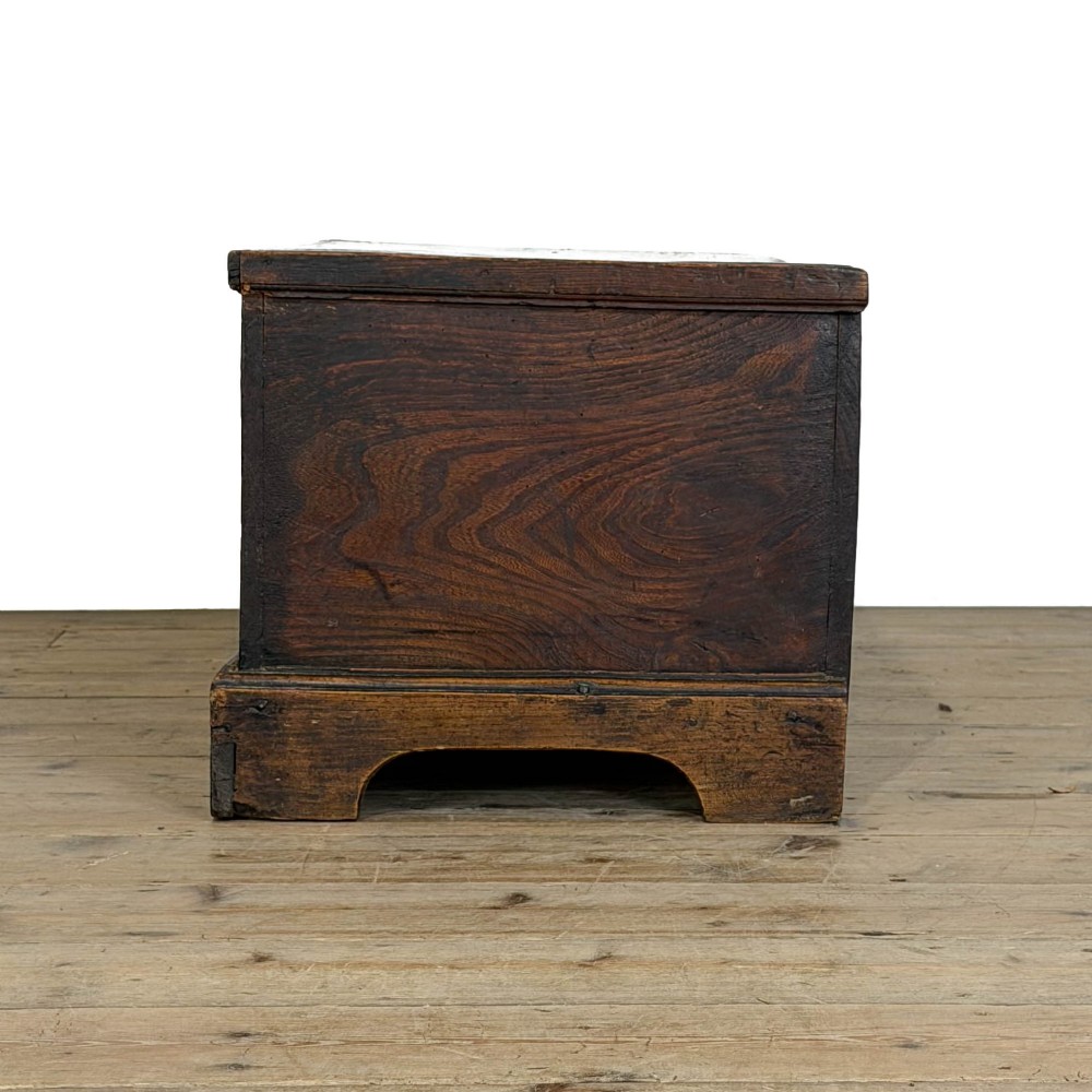 A rectangular George III dark elm blanket chest with a hinged lid, brass escutcheon, and bracket feet. View VI