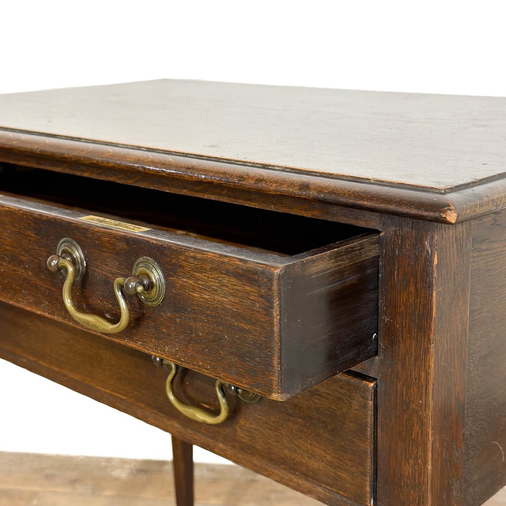 A dark oak lowboy table with two stacked drawers featuring brass drop handles and tapered square legs. View V