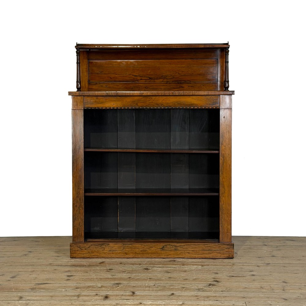 An antique rosewood open bookcase featuring a raised back gallery flanked by turned columns, with three open shelves and a beaded trim.