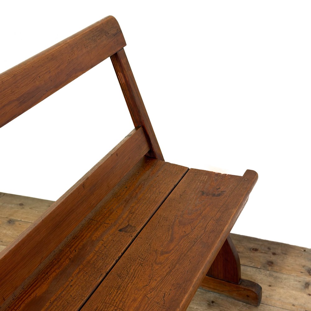 An antique pine bench featuring a pivoting backrest mechanism set above a long plank seat and shaped trestle end supports. View II