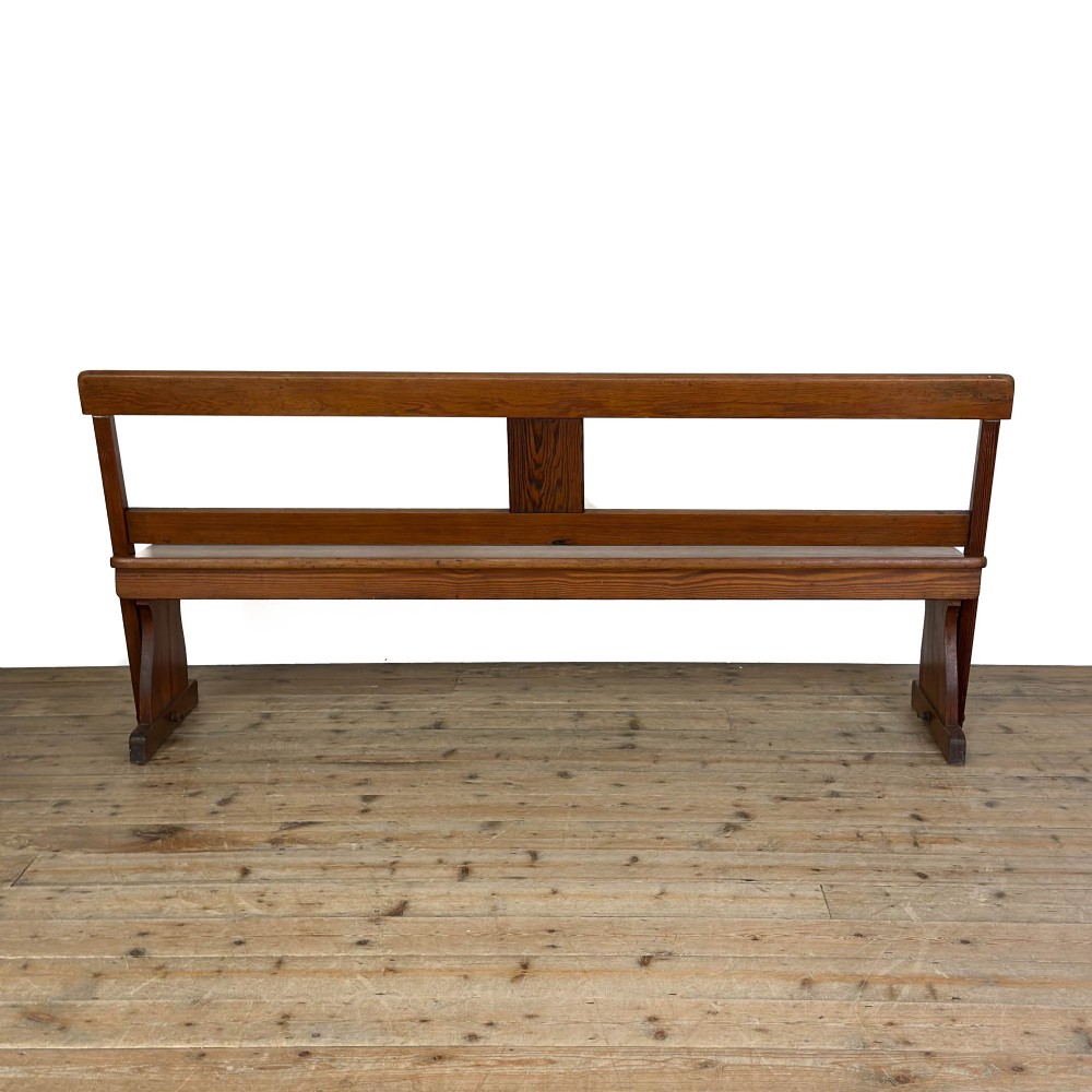 An antique pine bench featuring a pivoting backrest mechanism set above a long plank seat and shaped trestle end supports. View V