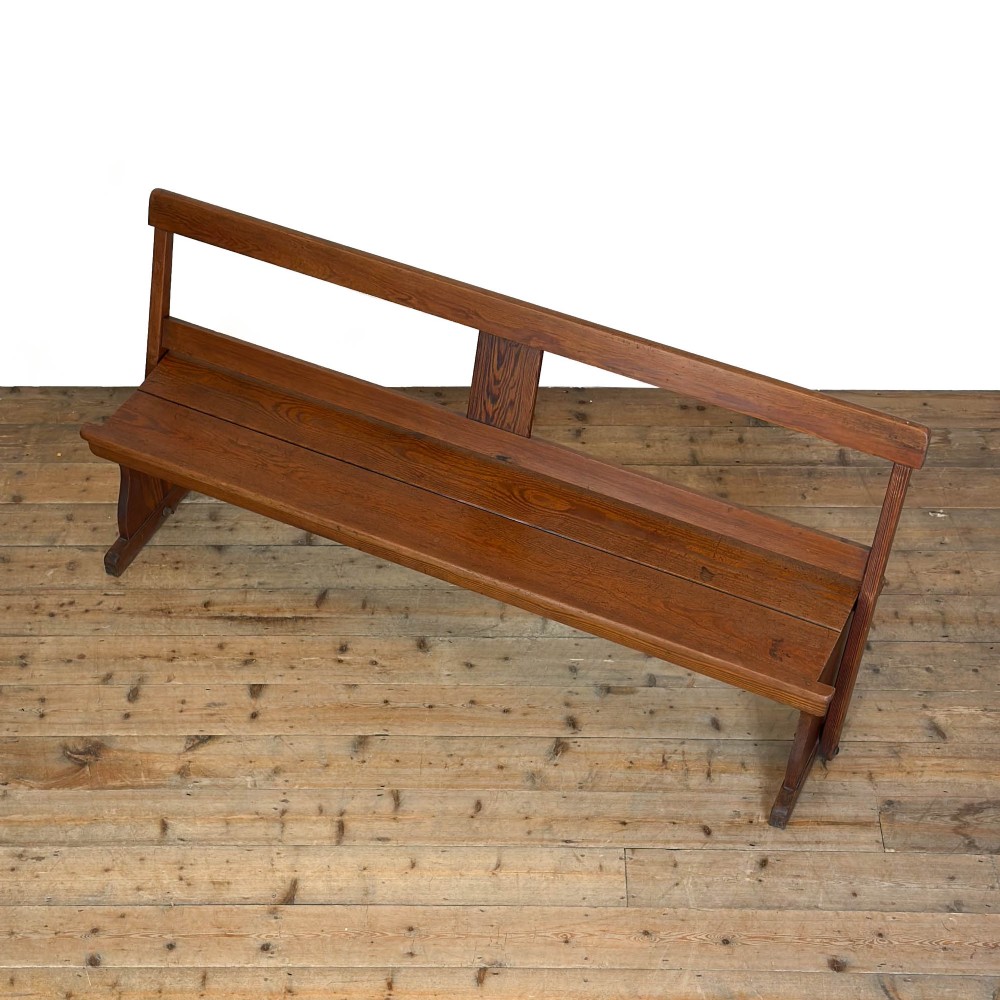 An antique pine bench featuring a pivoting backrest mechanism set above a long plank seat and shaped trestle end supports. View VI