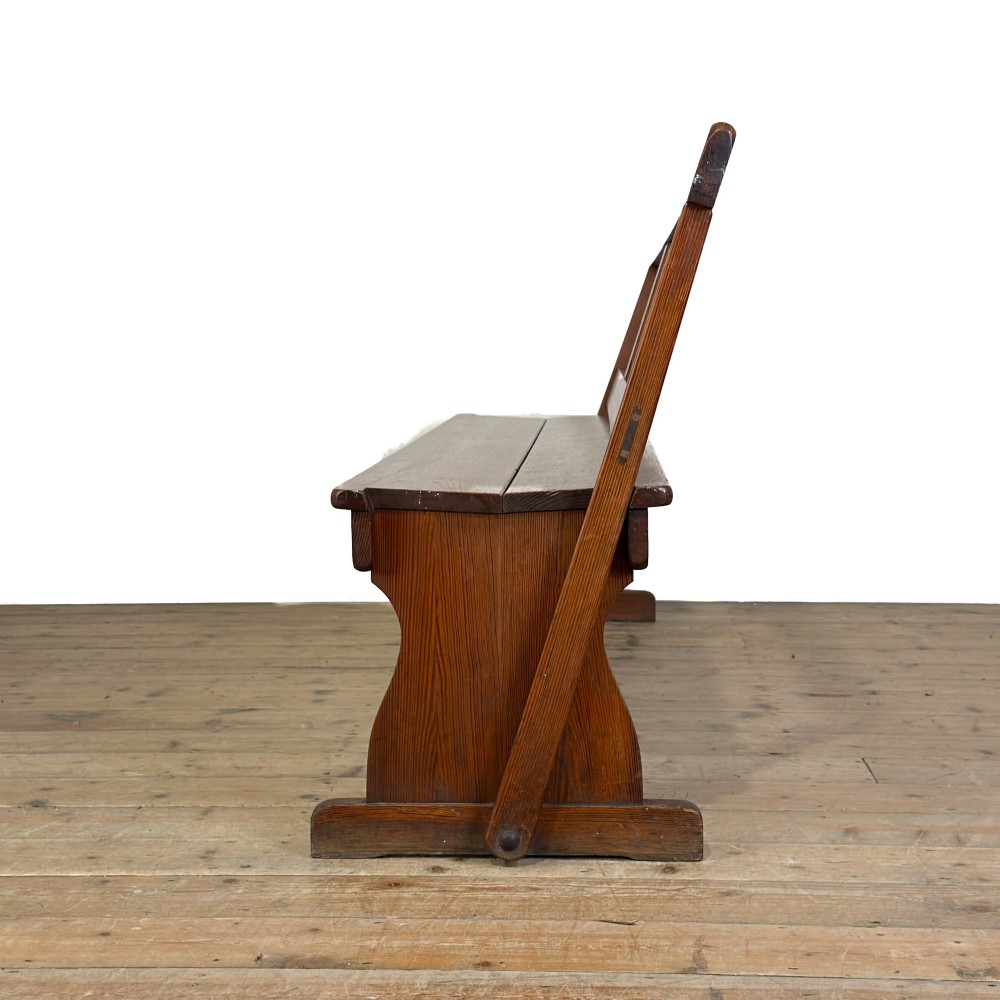 An antique pine bench featuring a pivoting backrest mechanism set above a long plank seat and shaped trestle end supports. View VIII
