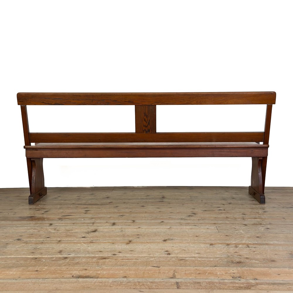An antique pine bench featuring a pivoting backrest mechanism set above a long plank seat and shaped trestle end supports. View IX