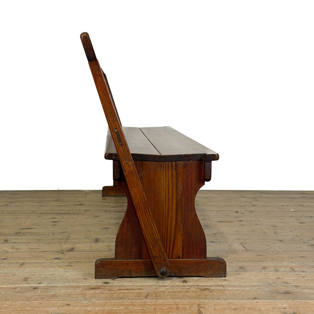 An antique pine bench featuring a pivoting backrest mechanism set above a long plank seat and shaped trestle end supports. View X