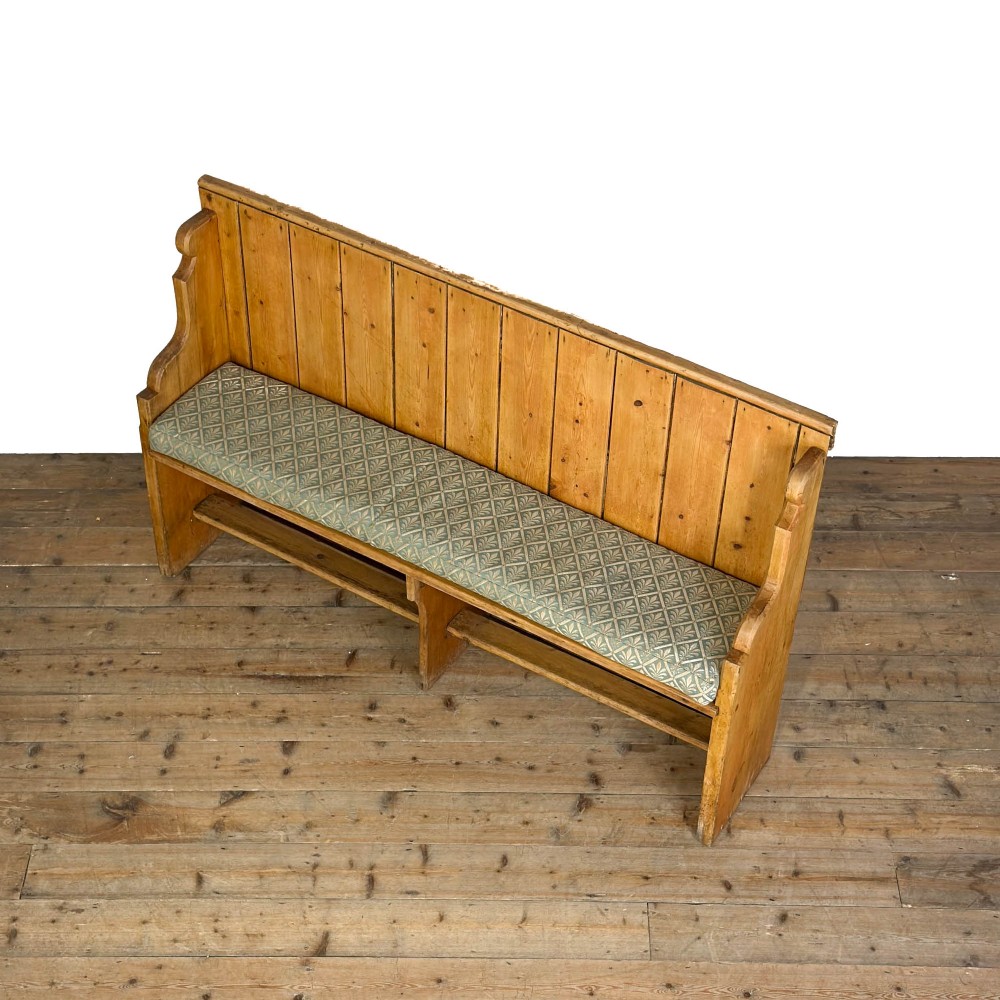 An antique pine church pew bench featuring a high vertical plank back, shaped scrolled side arms, a lower foot rail, and a patterned green fabric seat cushion. View IV