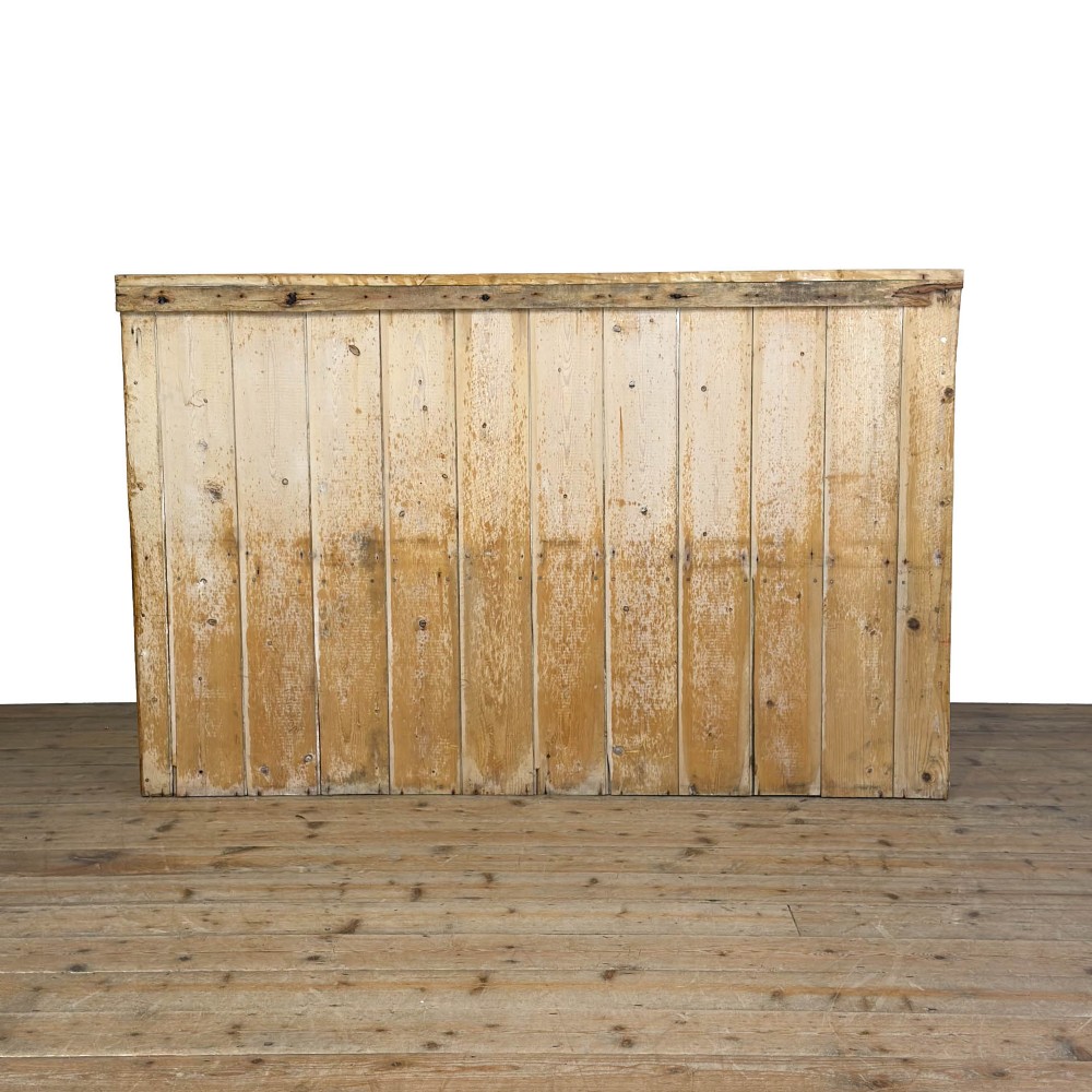 An antique pine church pew bench featuring a high vertical plank back, shaped scrolled side arms, a lower foot rail, and a patterned green fabric seat cushion. View VII