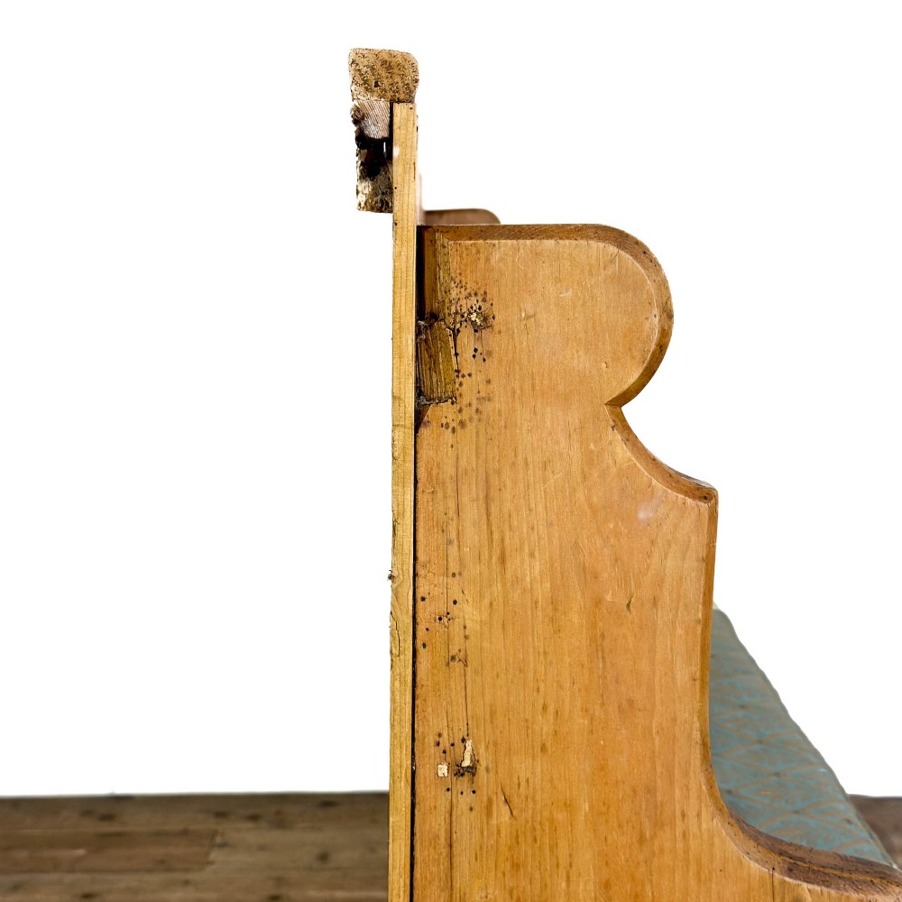 An antique pine church pew bench featuring a high vertical plank back, shaped scrolled side arms, a lower foot rail, and a patterned green fabric seat cushion. View IX