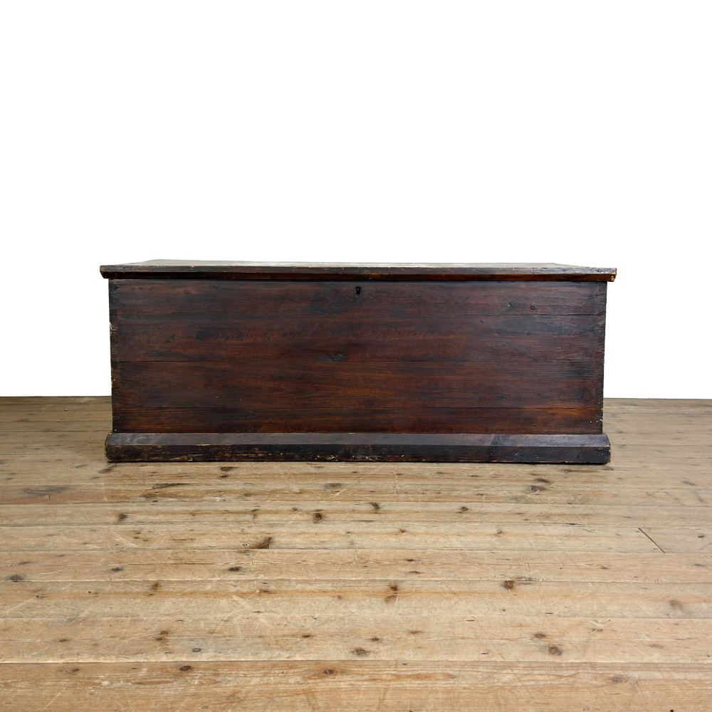 An antique stained pine blanket box featuring a flat hinged lid, dark wood finish, moulded plinth base, and central keyhole escutcheon.