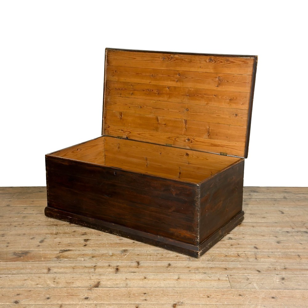 An antique stained pine blanket box featuring a flat hinged lid, dark wood finish, moulded plinth base, and central keyhole escutcheon. View VII