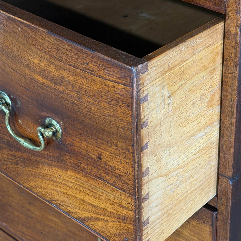 A four-drawer Georgian chest of drawers crafted from dark mahogany wood featuring brass swan-neck handles and bracket feet. View V