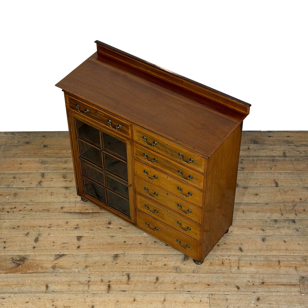 An Edwardian mahogany cabinet featuring an eight-pane glazed door on the left beside a vertical bank of six drawers with brass handles. View VI