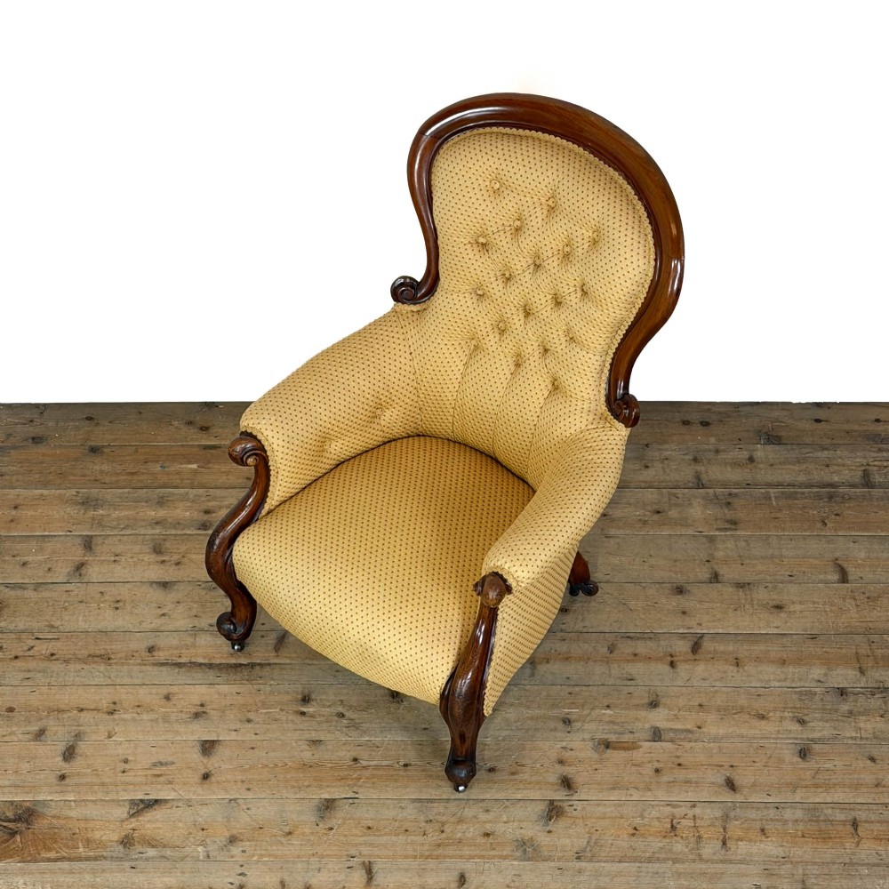 A Victorian upholstered armchair featuring a button-backed yellow patterned fabric seat and a carved mahogany frame with brass castors. View III