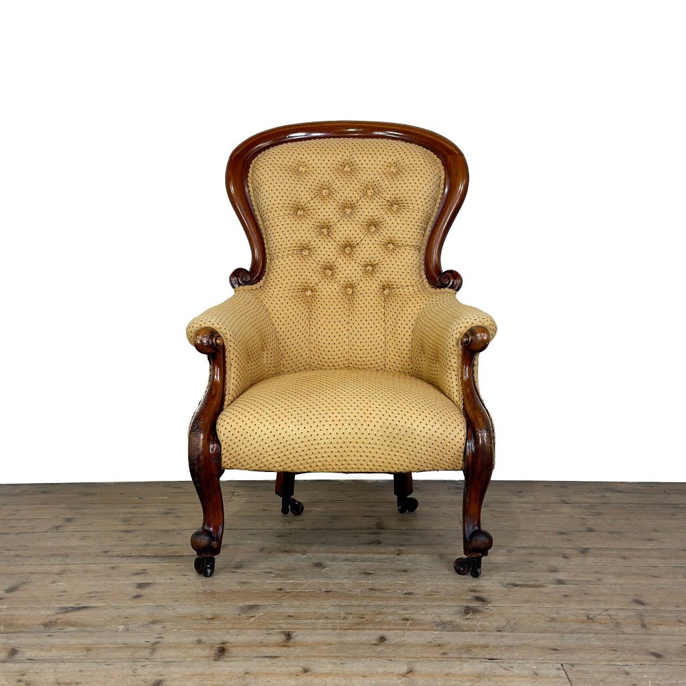 A Victorian upholstered armchair featuring a button-backed yellow patterned fabric seat and a carved mahogany frame with brass castors. View IV