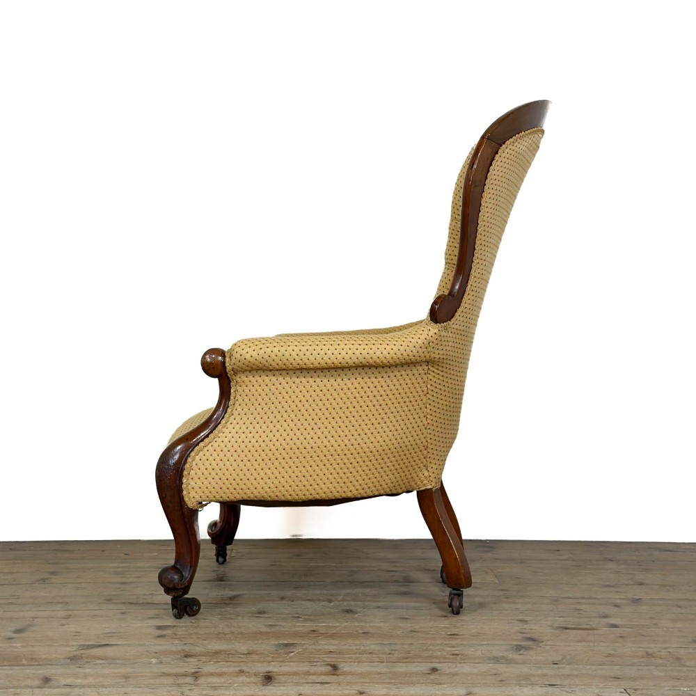 A Victorian upholstered armchair featuring a button-backed yellow patterned fabric seat and a carved mahogany frame with brass castors. View V