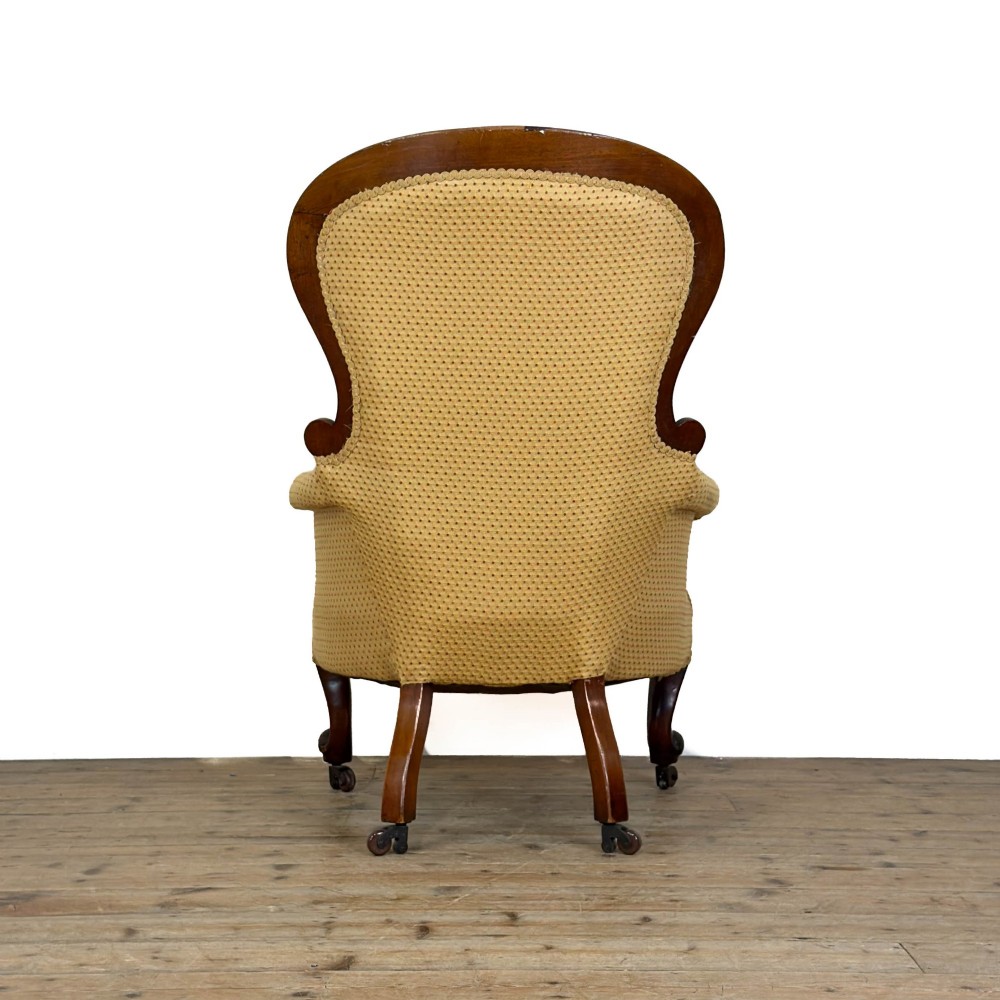 A Victorian upholstered armchair featuring a button-backed yellow patterned fabric seat and a carved mahogany frame with brass castors. View VI