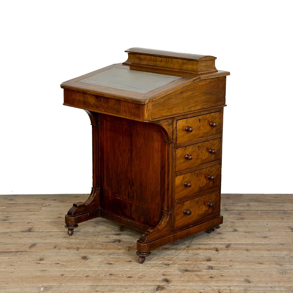 An antique Victorian walnut Davenport desk featuring a slanted leather-lined writing surface, an upper stationery compartment, and four drawers on the side.