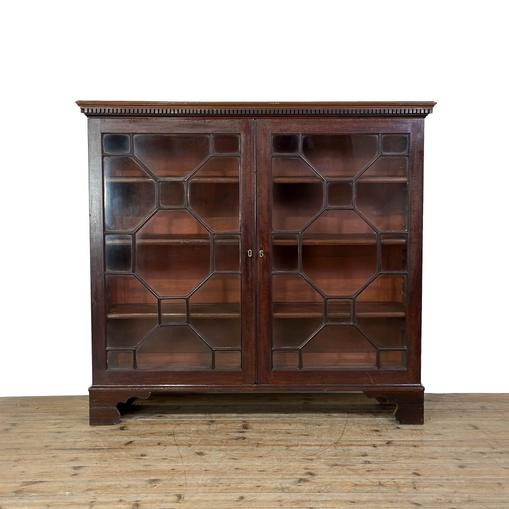 A 19th-century dark mahogany low bookcase featuring two glazed doors with geometric astragal glazing bars, dentil moulding at the top cornice, and bracket feet.
