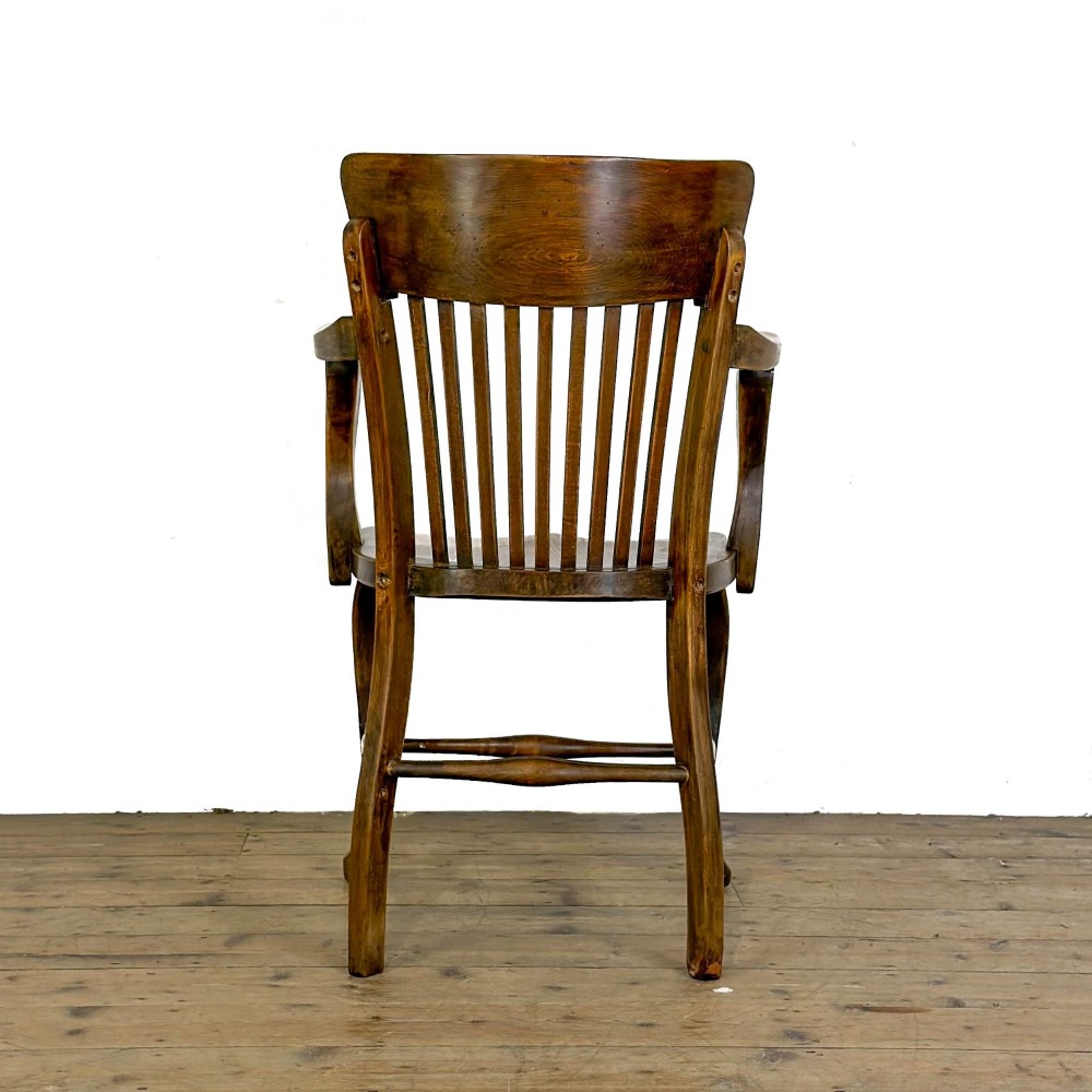 An antique warm brown oak office armchair with a slatted backrest, curved armrests, a contoured wooden seat, and turned legs. View II