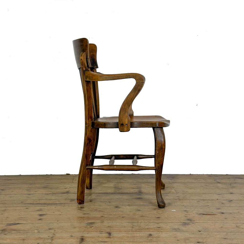 An antique warm brown oak office armchair with a slatted backrest, curved armrests, a contoured wooden seat, and turned legs. View III