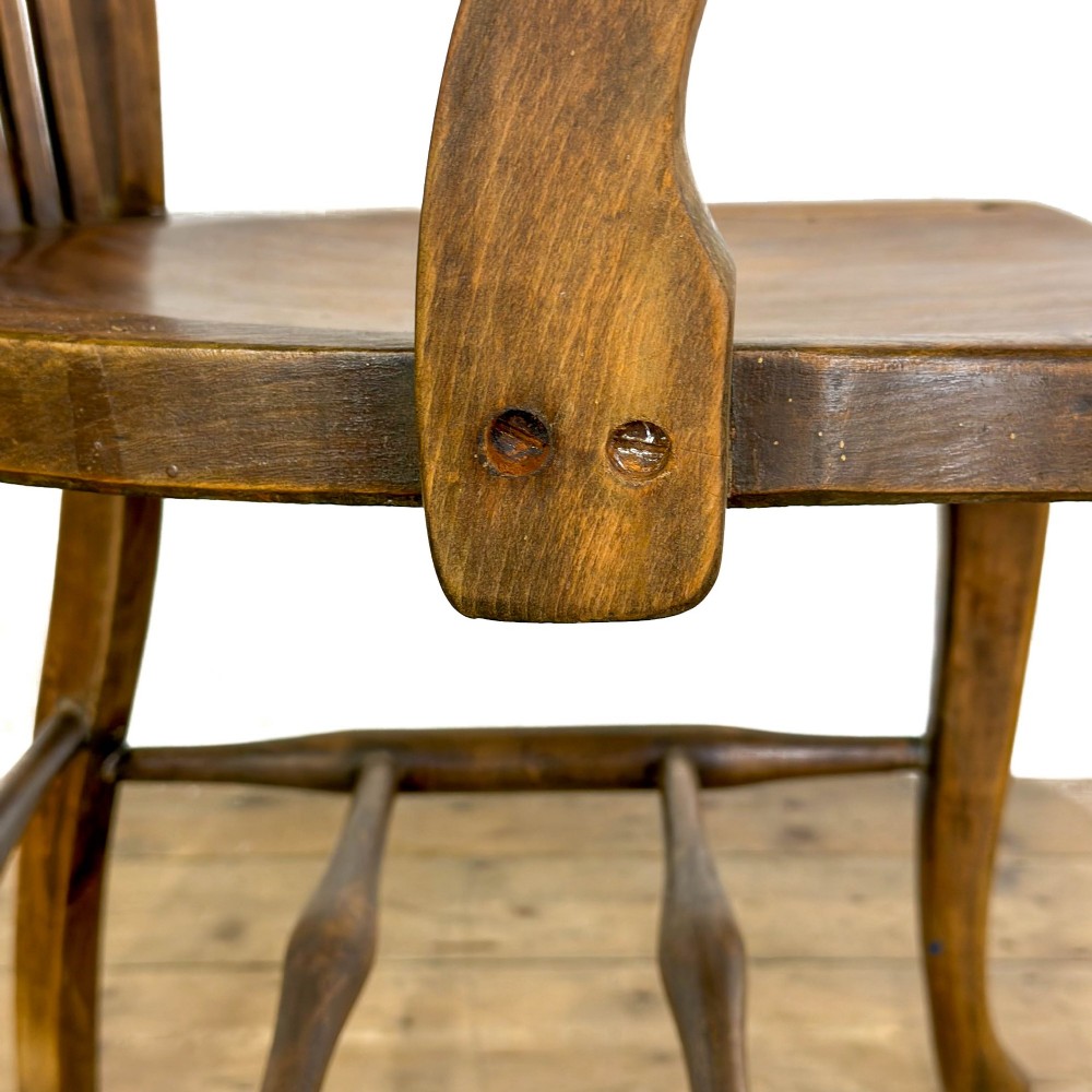 An antique warm brown oak office armchair with a slatted backrest, curved armrests, a contoured wooden seat, and turned legs. View V