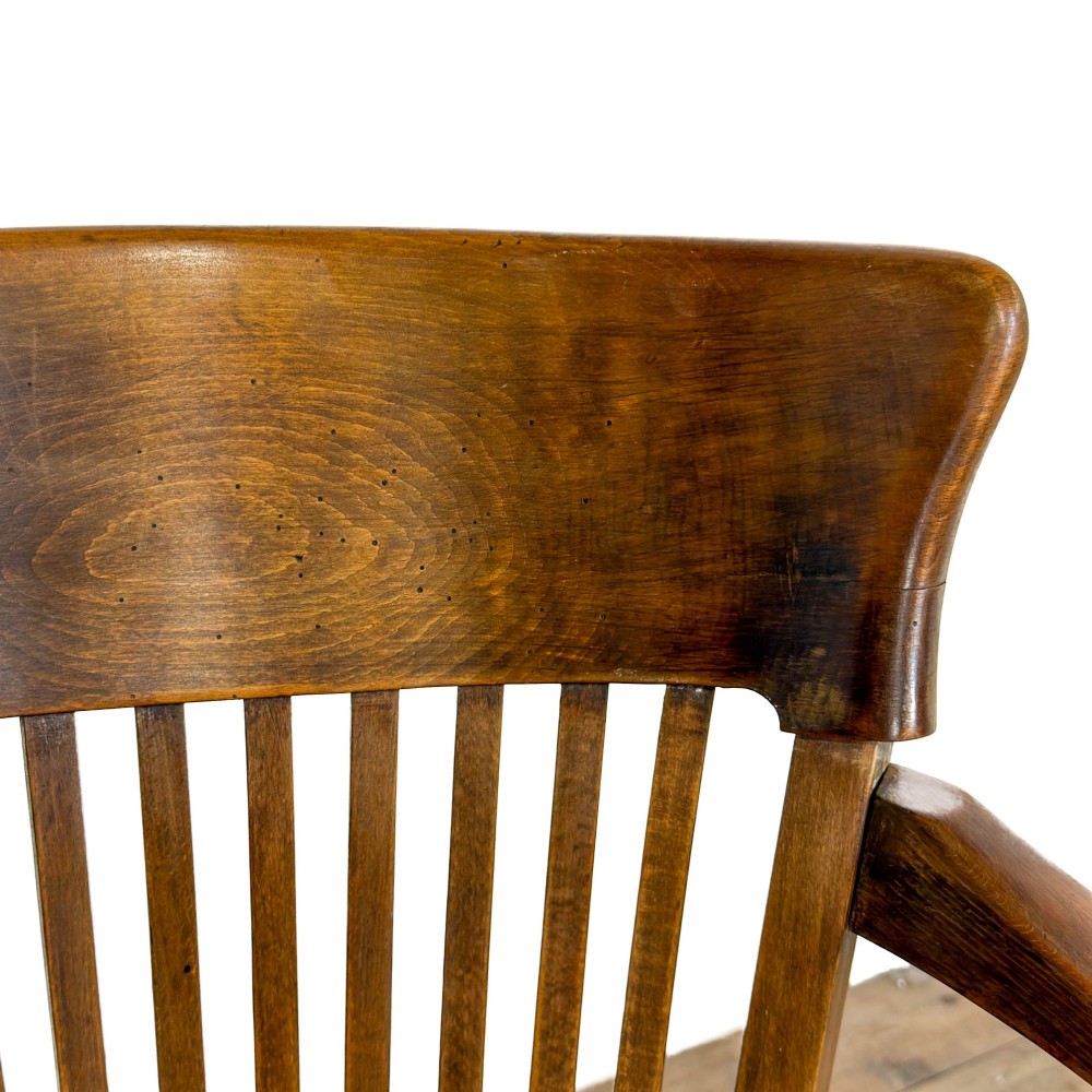 An antique warm brown oak office armchair with a slatted backrest, curved armrests, a contoured wooden seat, and turned legs. View VI
