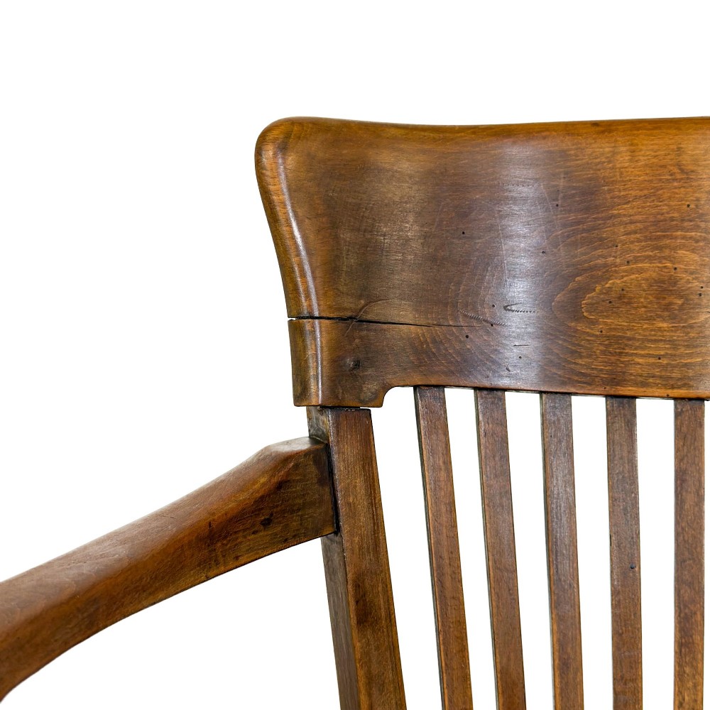 An antique warm brown oak office armchair with a slatted backrest, curved armrests, a contoured wooden seat, and turned legs. View VII