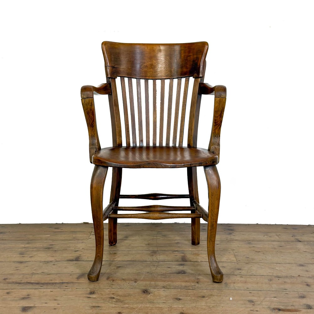 An antique warm brown oak office armchair with a slatted backrest, curved armrests, a contoured wooden seat, and turned legs. View VIII