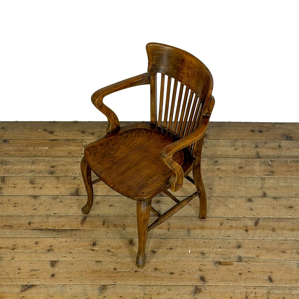 An antique warm brown oak office armchair with a slatted backrest, curved armrests, a contoured wooden seat, and turned legs. View IX