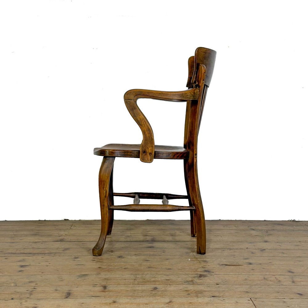 An antique warm brown oak office armchair with a slatted backrest, curved armrests, a contoured wooden seat, and turned legs. View X